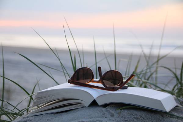 Quelle: BEK (Bremische Evangelische Kirche) / fundus-medien.de, Fundus, redaktionell frei verwendbar, 5117 Ein aufgeklapptes Buch liegt im Sand, am Strand. Darauf liegt eine Sonnenbrille, im Hintergrund ist das Meer und ein Sonnenuntergang sichtbar. Schöne Stimmung.